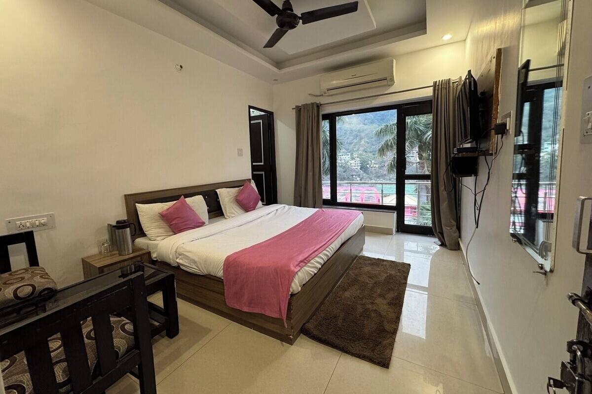 A modern bedroom with a large bed, a ceiling fan, an air conditioning unit, a TV mounted on the wall, and a view of palm trees through the window.