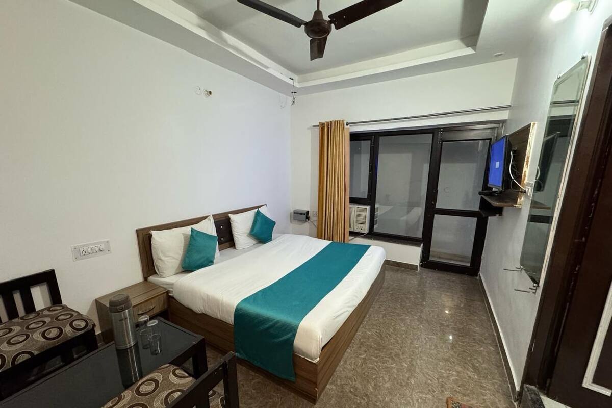 A hotel room with a bed, a desk, a chair, a ceiling fan, a TV, and a sliding door to a balcony.