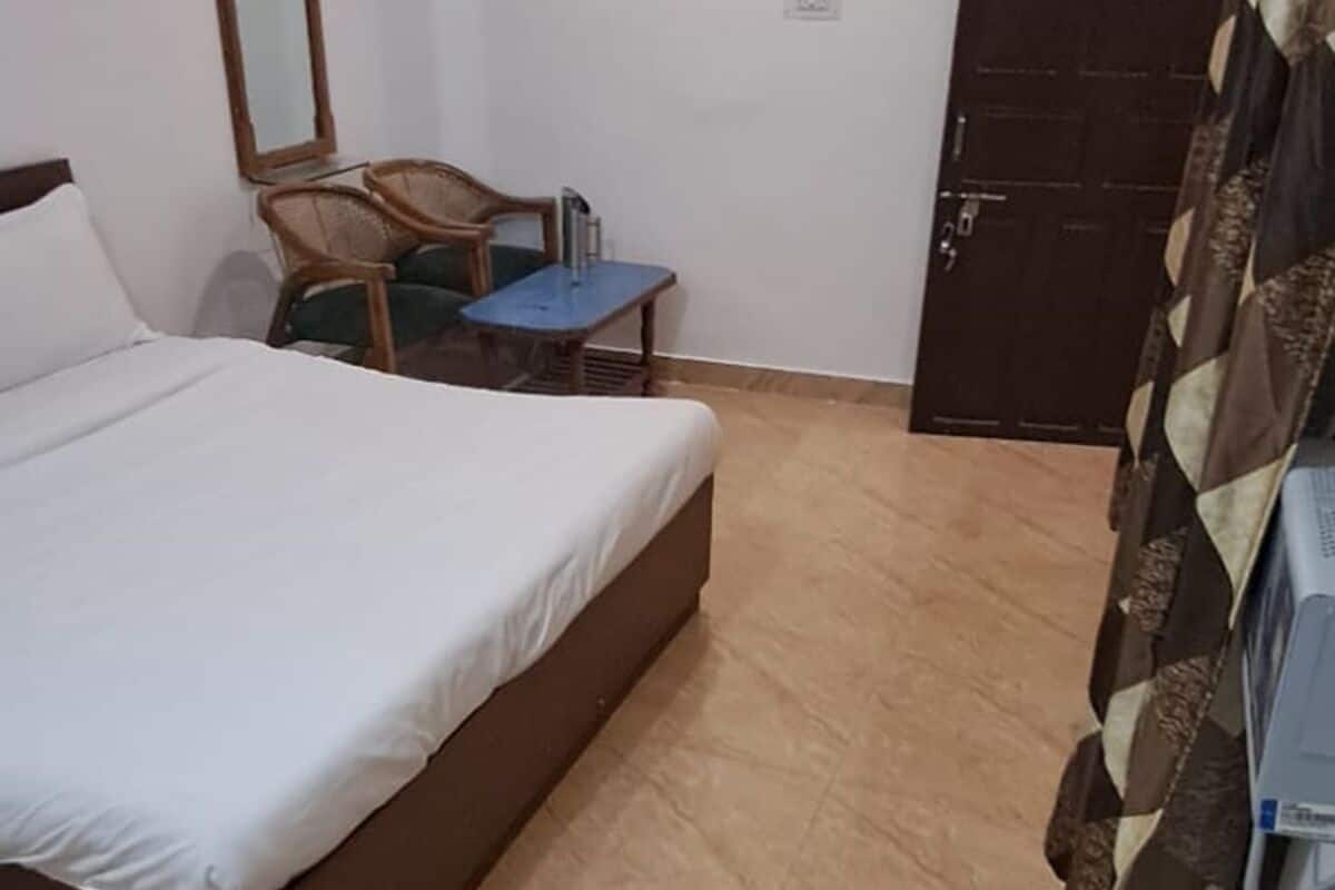 A bedroom with a bed, a chair, a small table, a mirror, and a door.