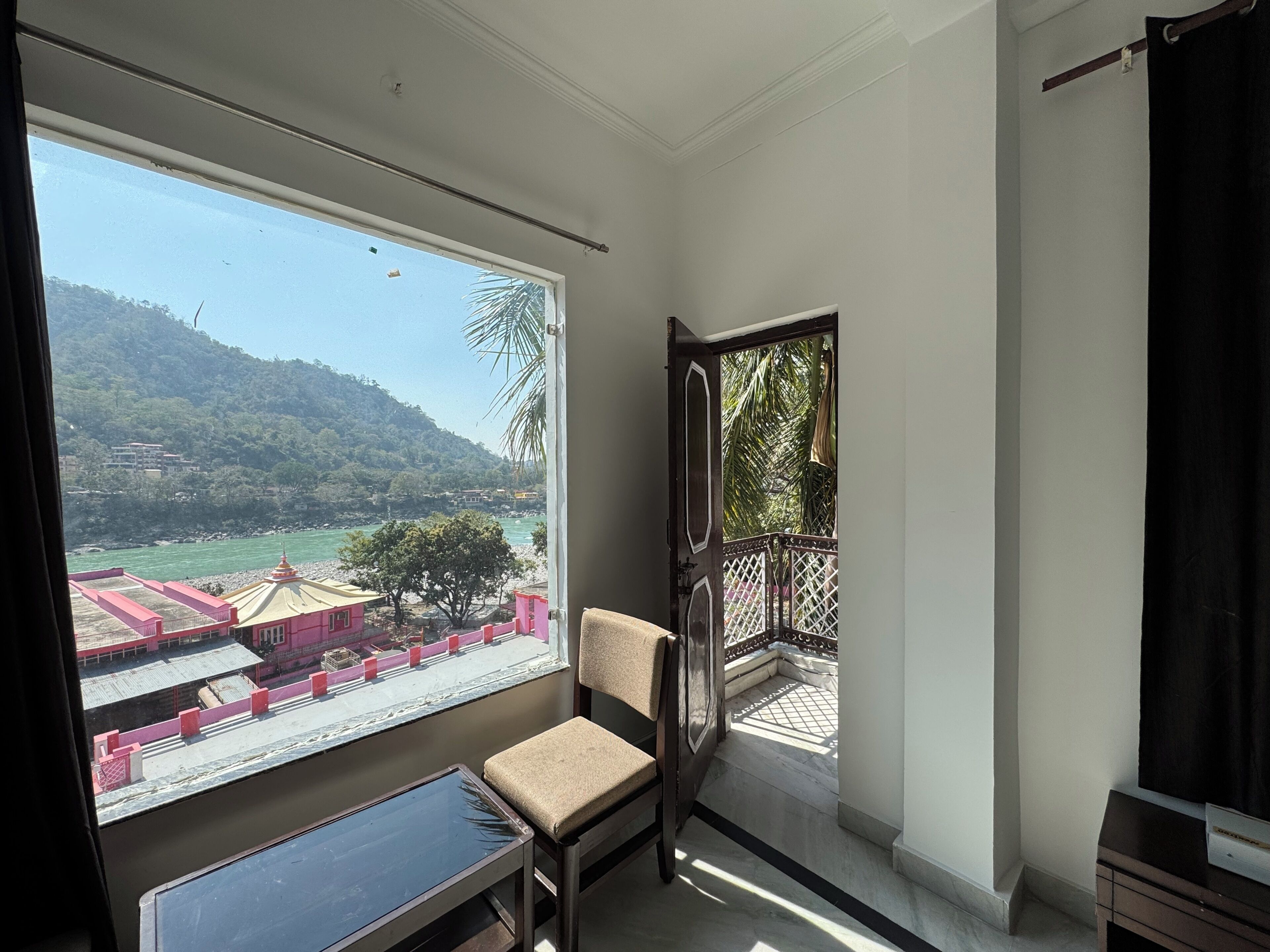 A room with a large window offering a view of a river and hills. There is a chair and a small table in the room.