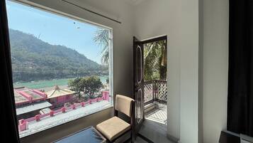 A room with a large window offering a view of a river and hills. There is a chair and a small table in the room.