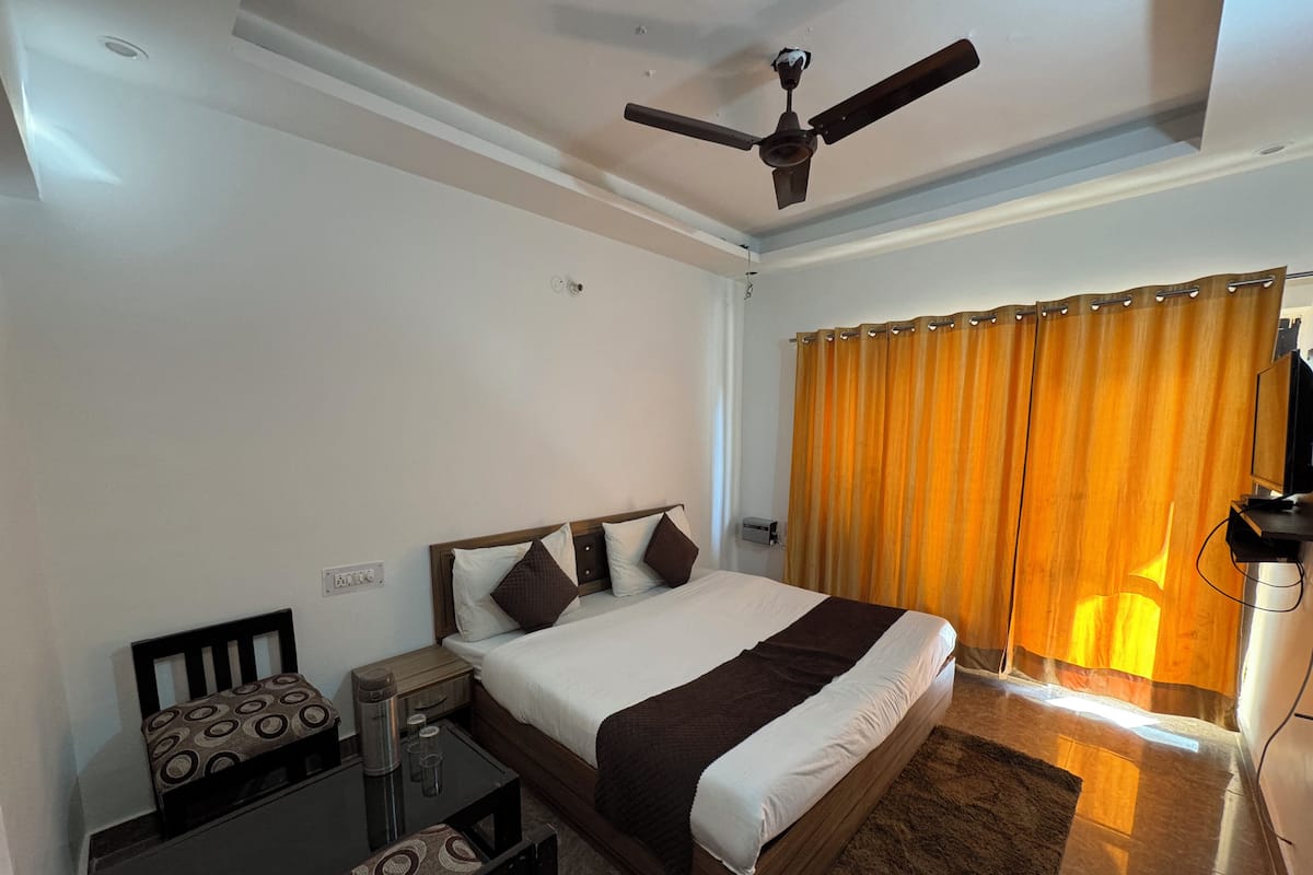 A hotel room with a bed, a desk, a chair, a coffee maker, a TV, and a ceiling fan.