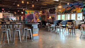 A spacious cafe with high ceilings, exposed beams, and a mural on the wall. There are multiple seating areas with stools and tables, and a bar counter with stools. - Urban Cottage. Walkable. Sweet Spring Stay (Austin)