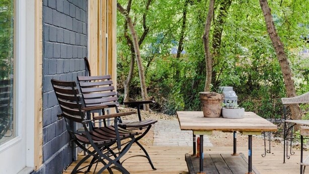 A wooden deck with a table and chairs, a doormat, and a potted plant. - Urban Cottage. Walkable. Sweet Spring Stay (Austin)
