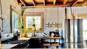 A kitchen with a wooden countertop, a gas stove, a stainless steel refrigerator, hanging plants, and shelves with cups and mugs. - Urban Cottage. Walkable. Sweet Spring Stay (Austin)
