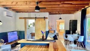A modern living room with a wooden floor, a central seating area, a TV, and a dining table with chairs. - Urban Cottage. Walkable. Sweet Spring Stay (Austin)