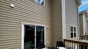 A deck with two chairs and a table, a sliding glass door, and a wooden railing. - The Cedar at Ducks Landing (Aberdeen)