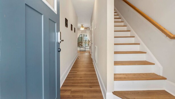 A hallway with a blue door, wooden stairs, and a ceiling fan. - The Cedar at Ducks Landing (Aberdeen)