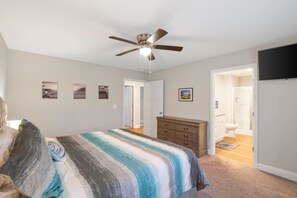 A bedroom with a bed, a dresser, a ceiling fan, and a door leading to a bathroom. - The Cedar at Ducks Landing (Aberdeen)