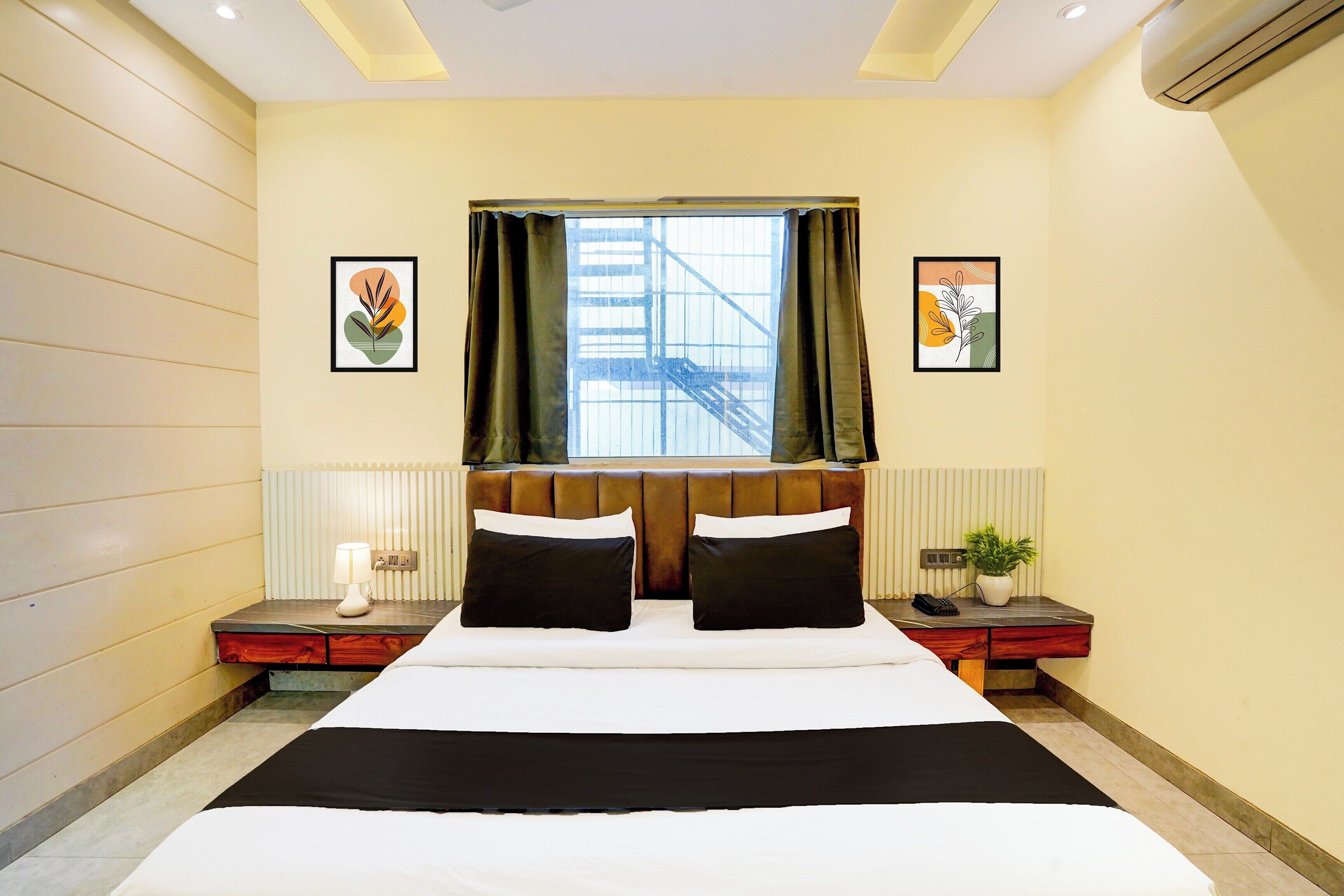 Ein Hotelzimmer mit einem großen Bett, zwei Nachttischen, einem Fenster mit Vorhängen und Bildern an den Wänden.