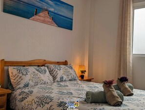 A bed with floral bedding, a wooden headboard, and a painting of a pier over water.