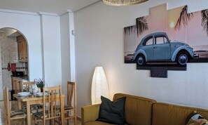 A dining area with a table set for four, a sofa, and a wall-mounted car poster.