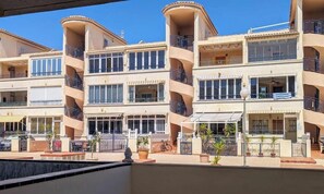 A multi-story hotel with balconies, a swimming pool, and potted plants.