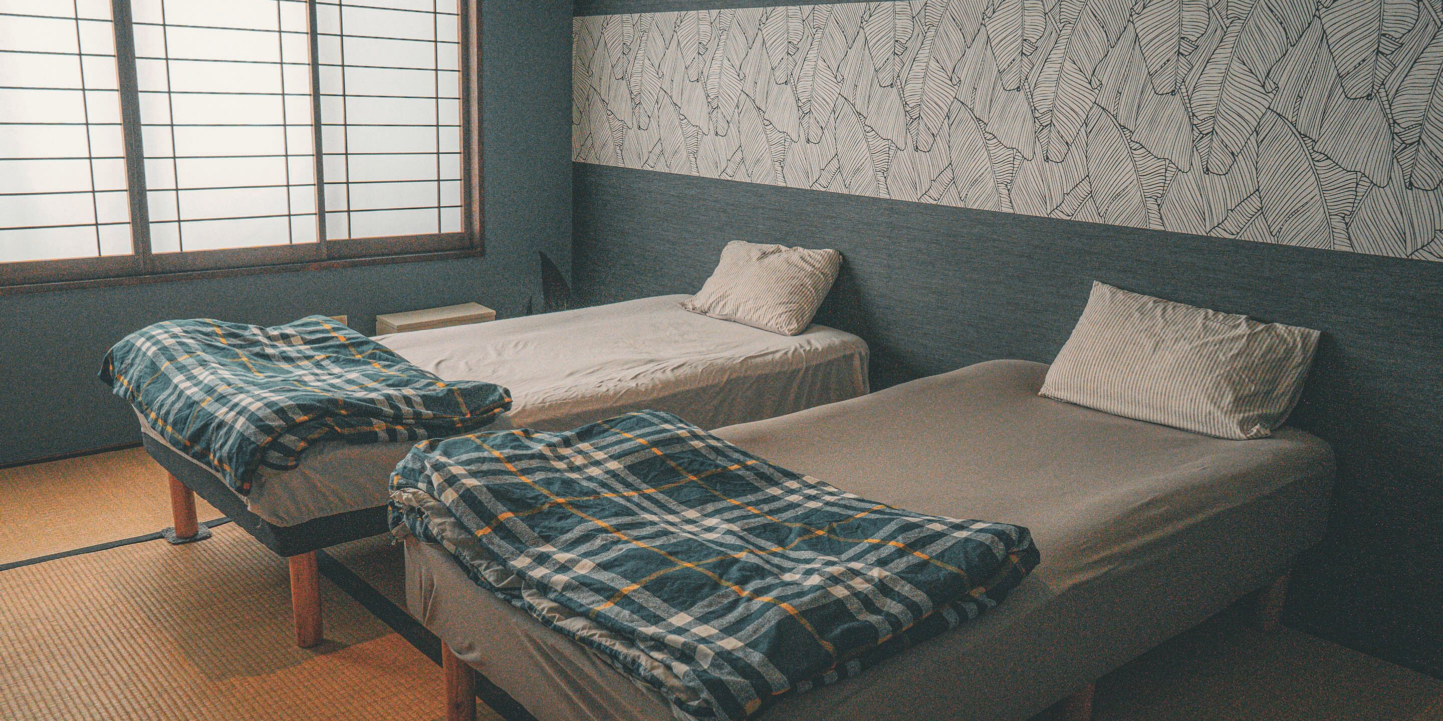Una habitación con dos camas individuales, una ventana con persianas y un papel tapiz estampado.