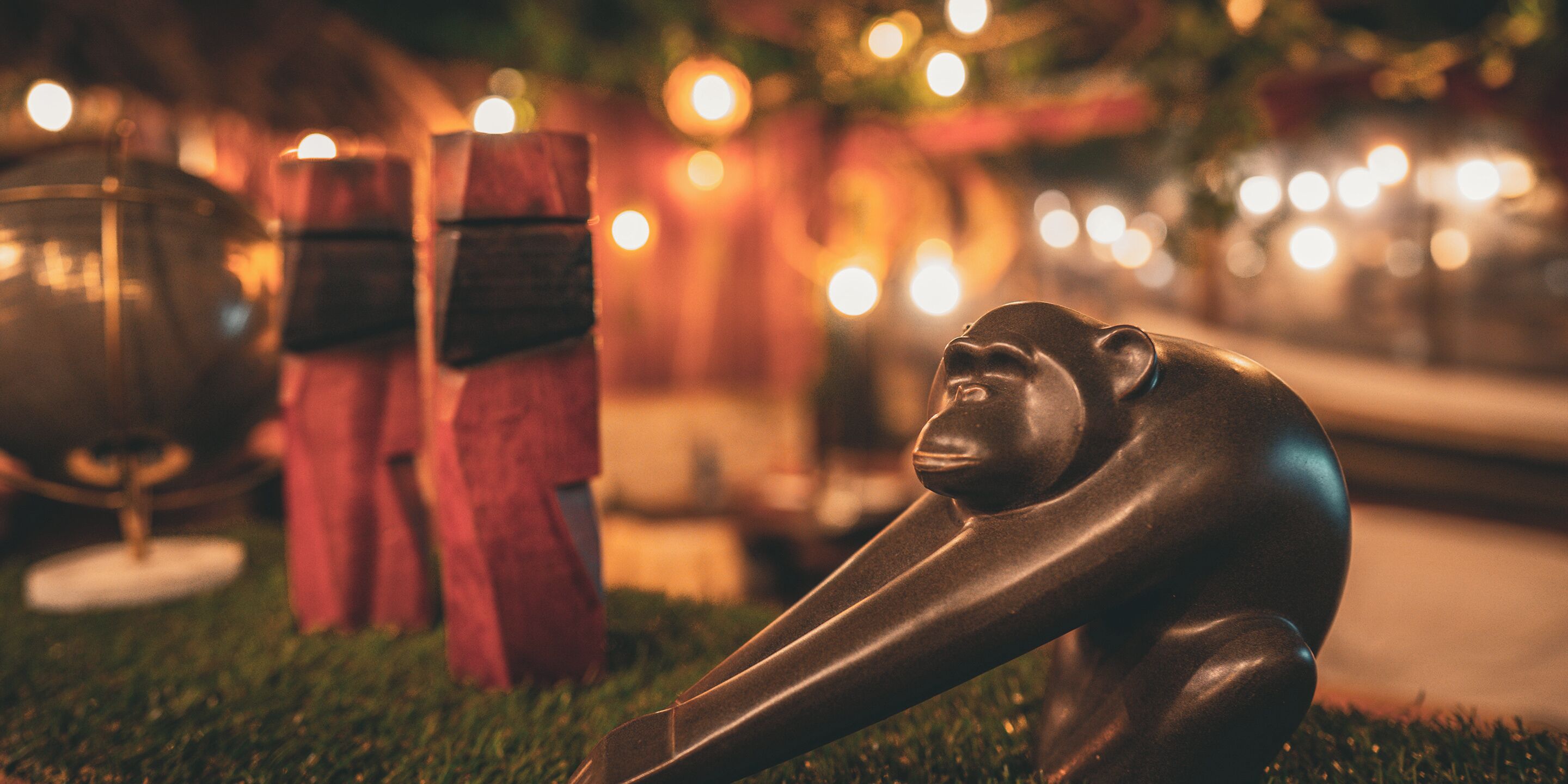 A sculpture of a monkey on grass with blurred lights in the background.