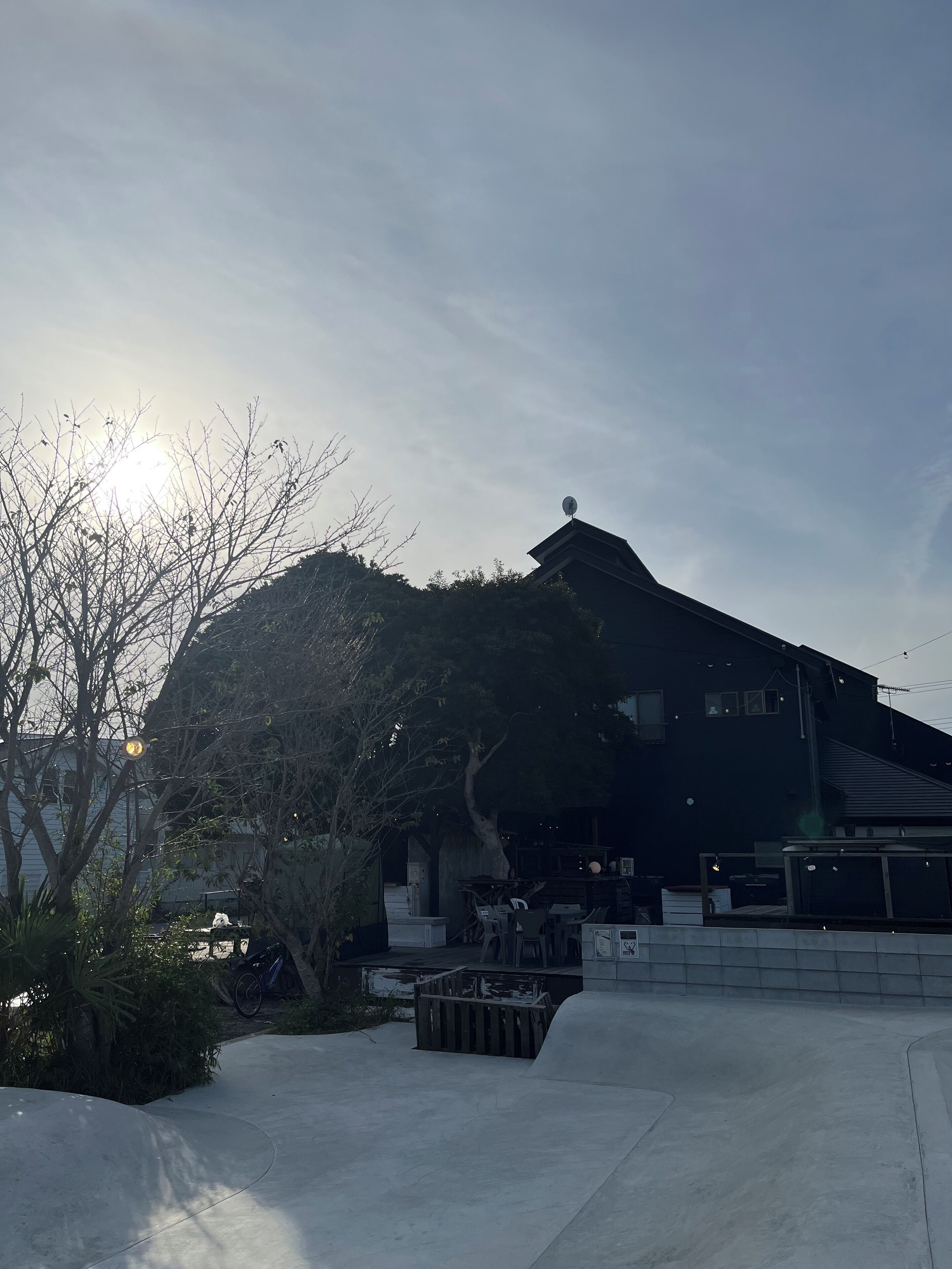 A modern building with a flat roof and satellite dish, surrounded by trees and a concrete area with benches.