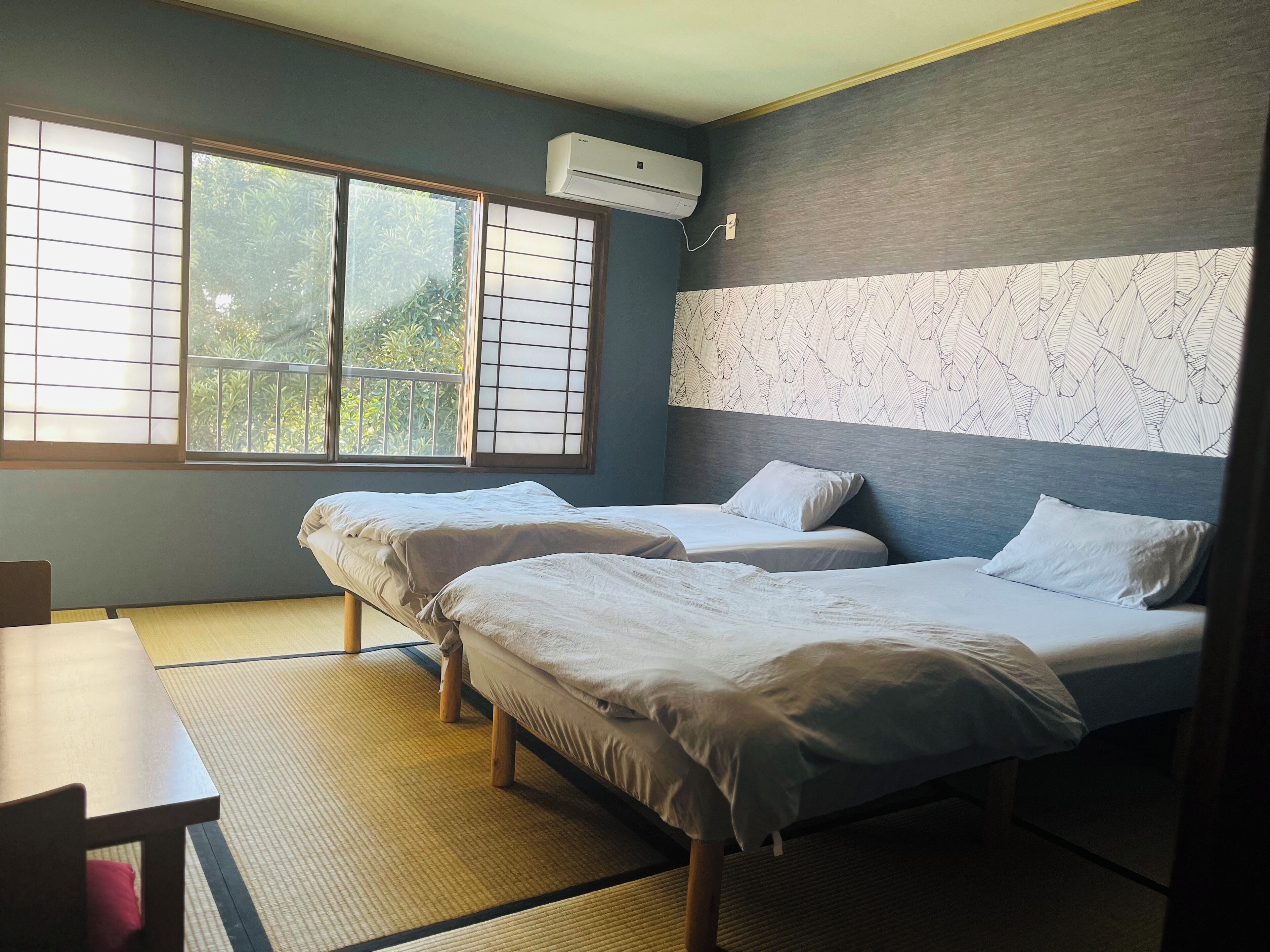 Une chambre avec deux lits, une table et une fenêtre avec des stores.