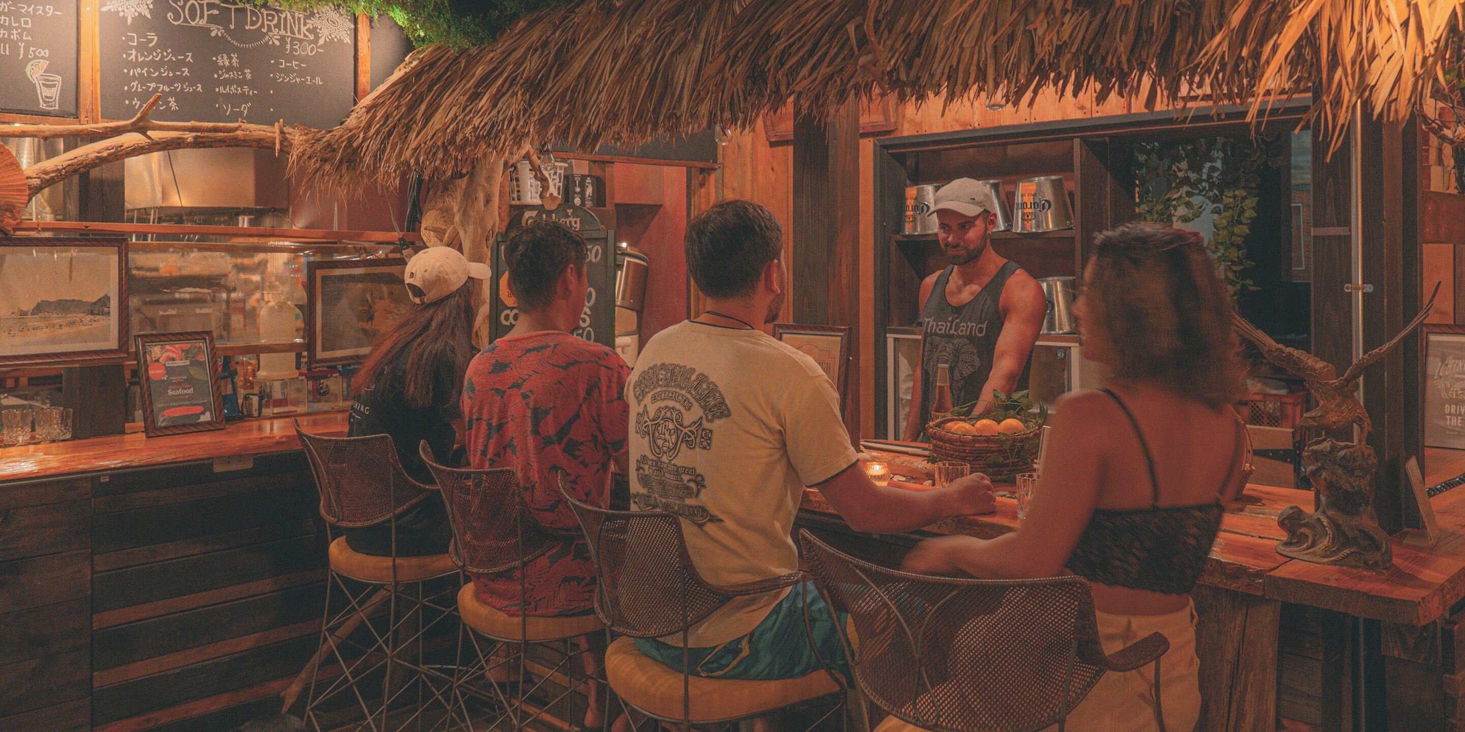 Een bar met houten meubels, een rieten dak en een menubord.