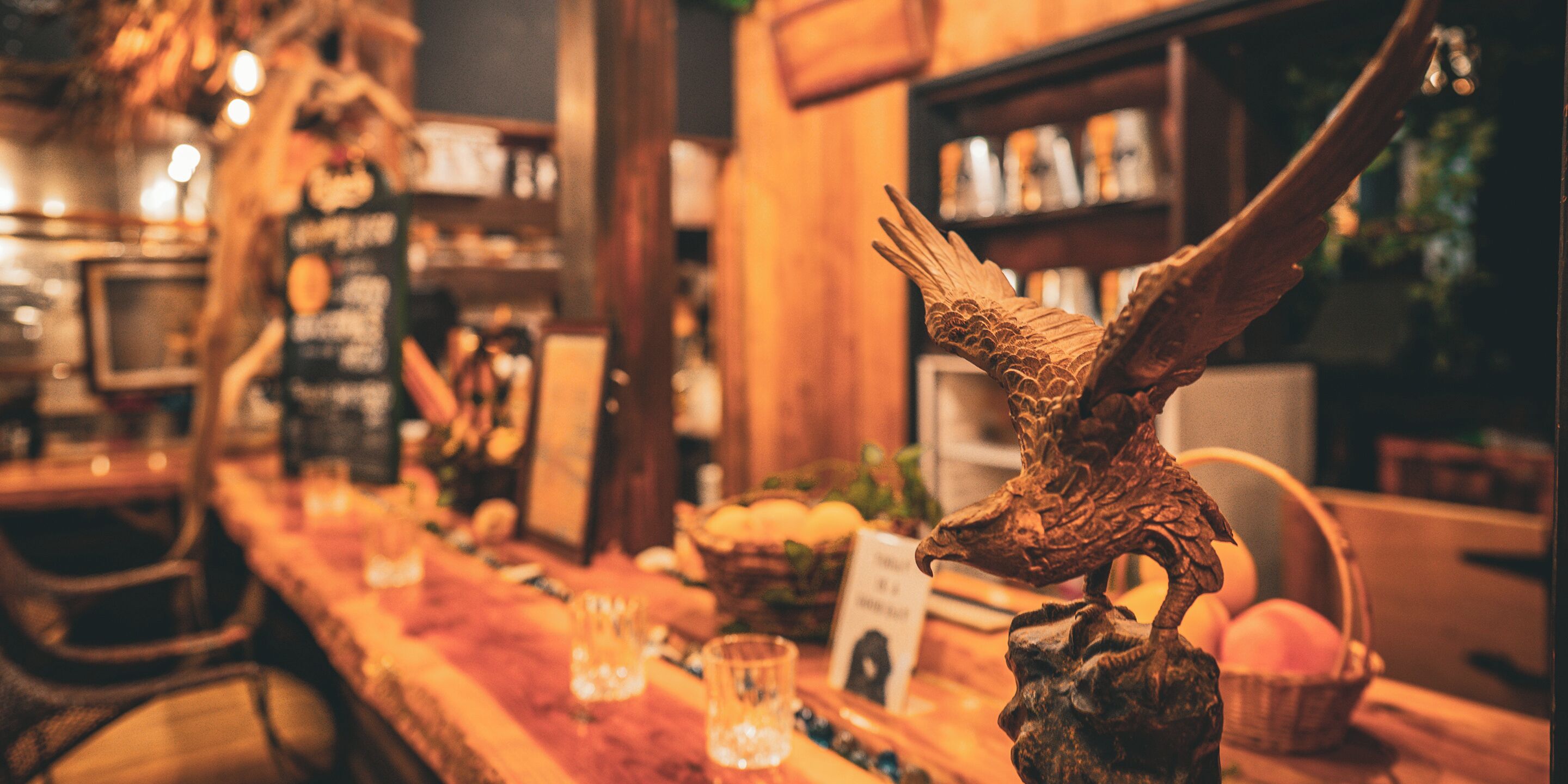 Un bar con arredi in legno, una scultura di un uccello appesa al muro e un espositore di frutta.