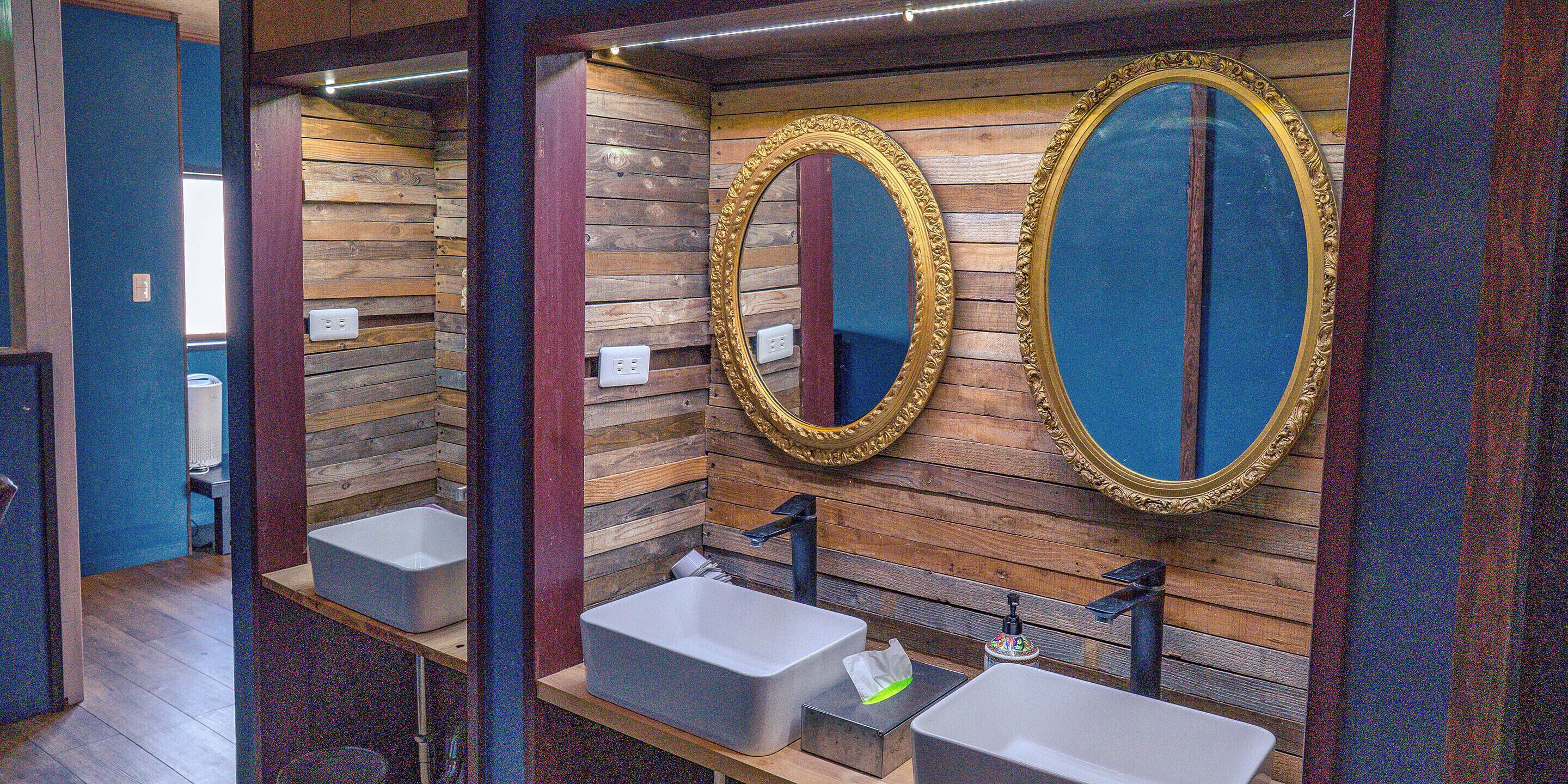 A bathroom with wooden panel walls, two sinks with gold-framed mirrors, and a blue accent wall.