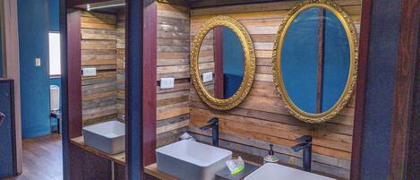 A bathroom with wooden panel walls, two sinks with gold-framed mirrors, and a blue accent wall.