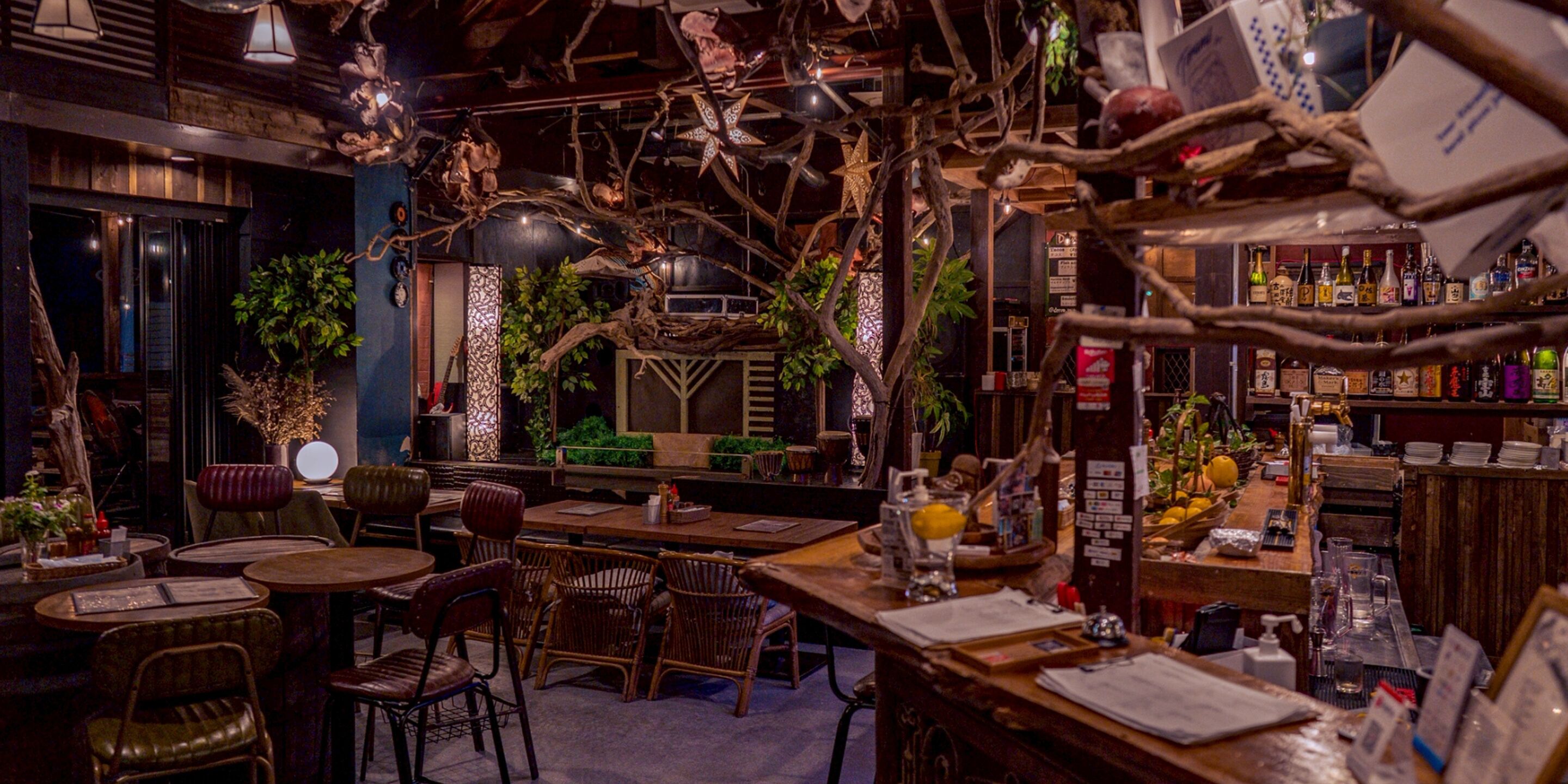 Un rincón acogedor de bar con mobiliario de madera, varias botellas en estantes y ramas decorativas en el techo.
