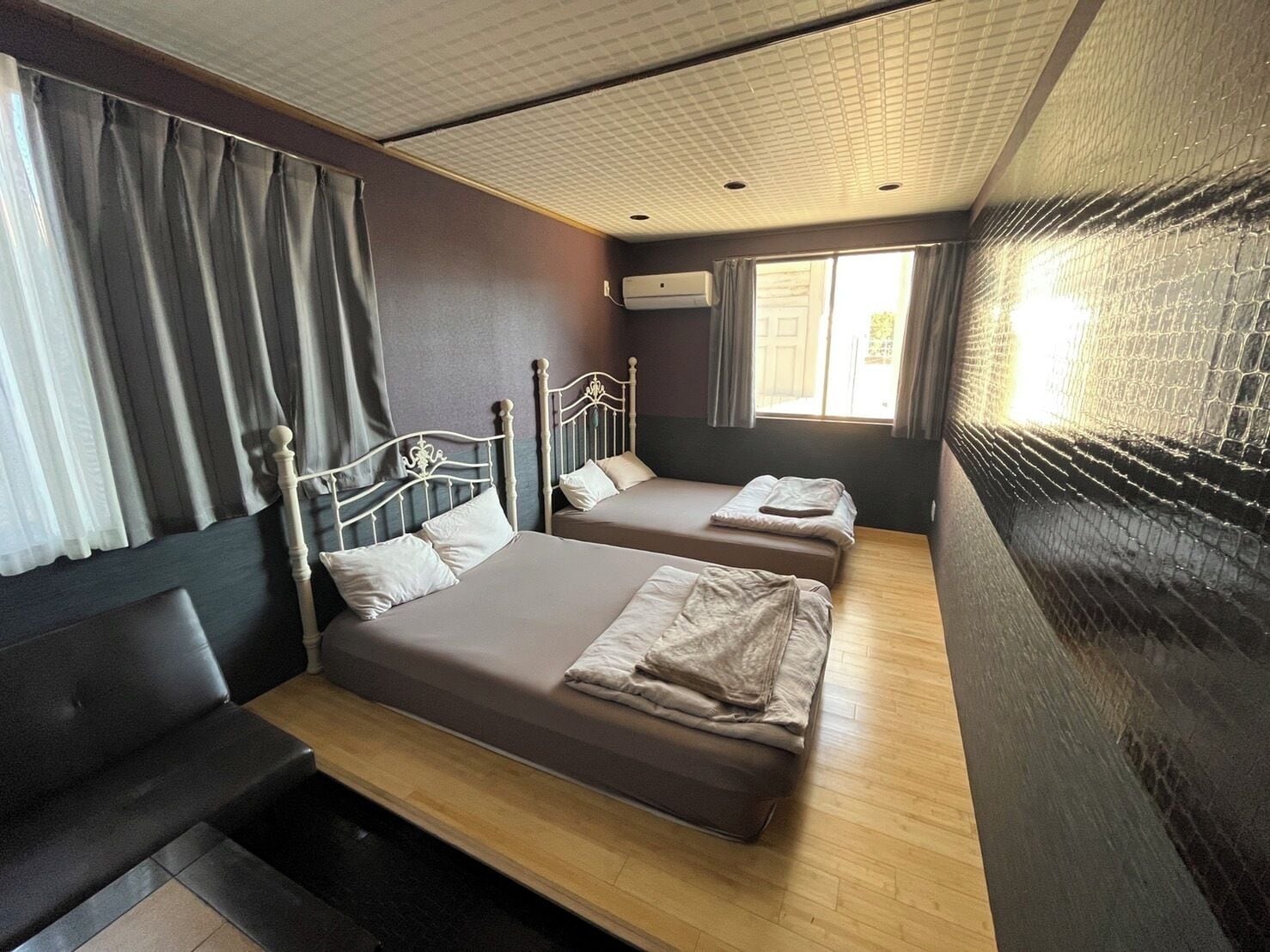 Una habitación con dos camas, un banco y una ventana con cortinas.