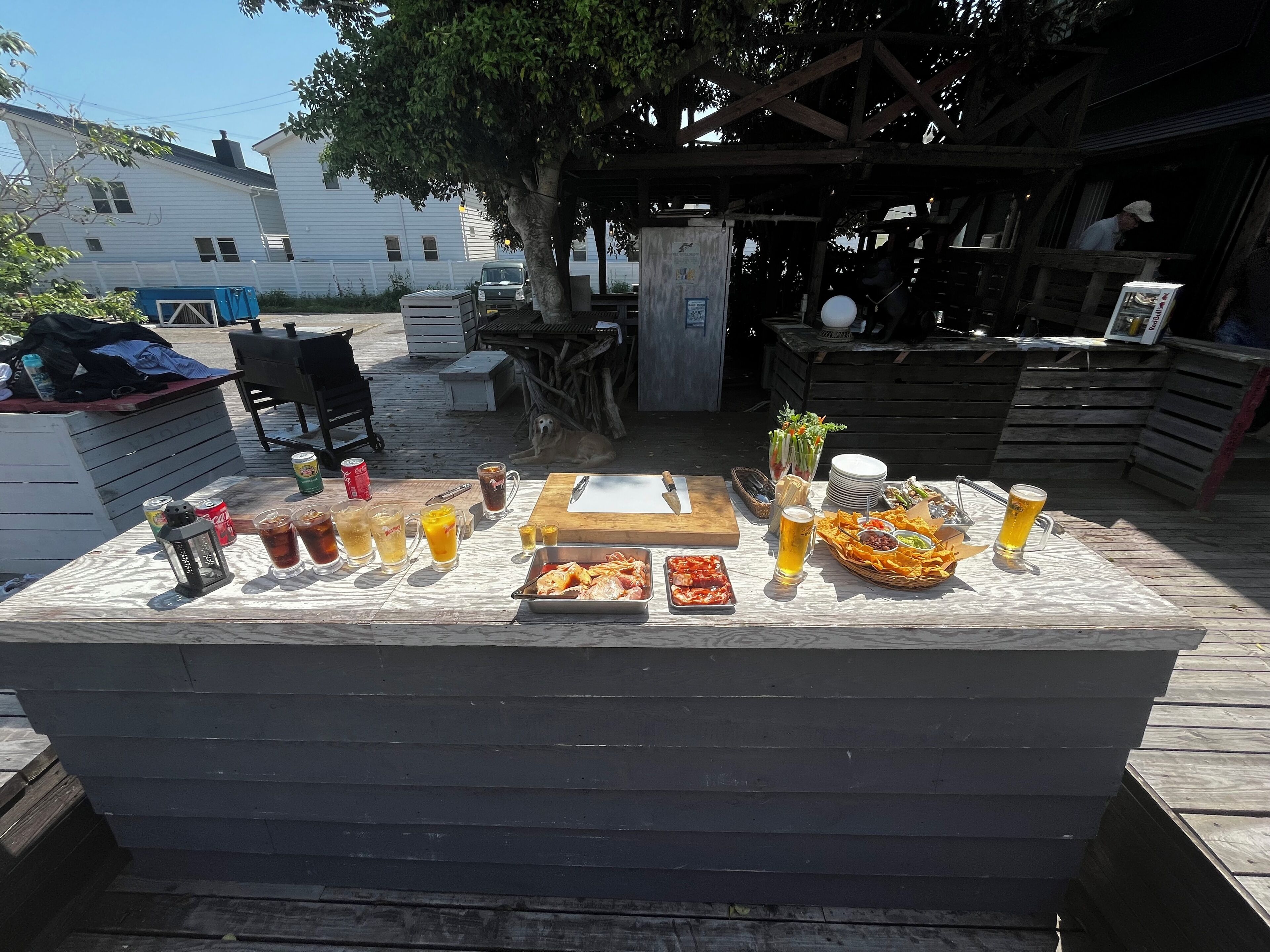 Un área de comedor al aire libre con una mesa de madera dispuesta para una comida, que incluye varios platos y bebidas.