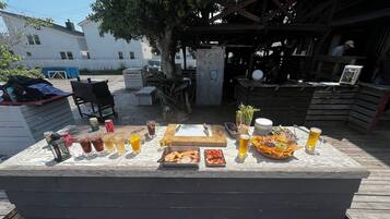 Un área de comedor al aire libre con una mesa de madera dispuesta para una comida, que incluye varios platos y bebidas.