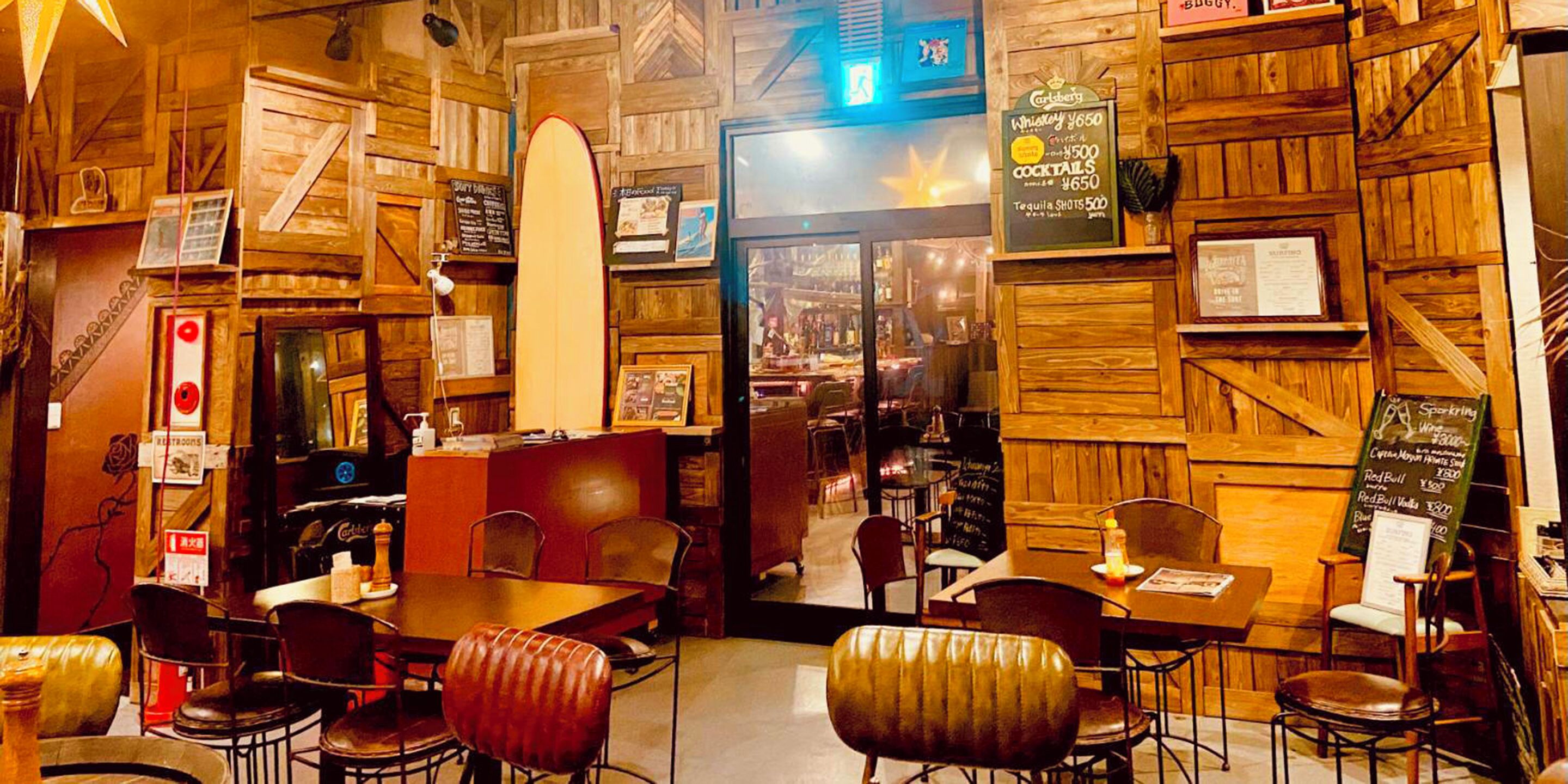 Un restaurante acogedor con paredes de madera y una decoración con tabla de surf. Mesas y sillas dispuestas para comer.