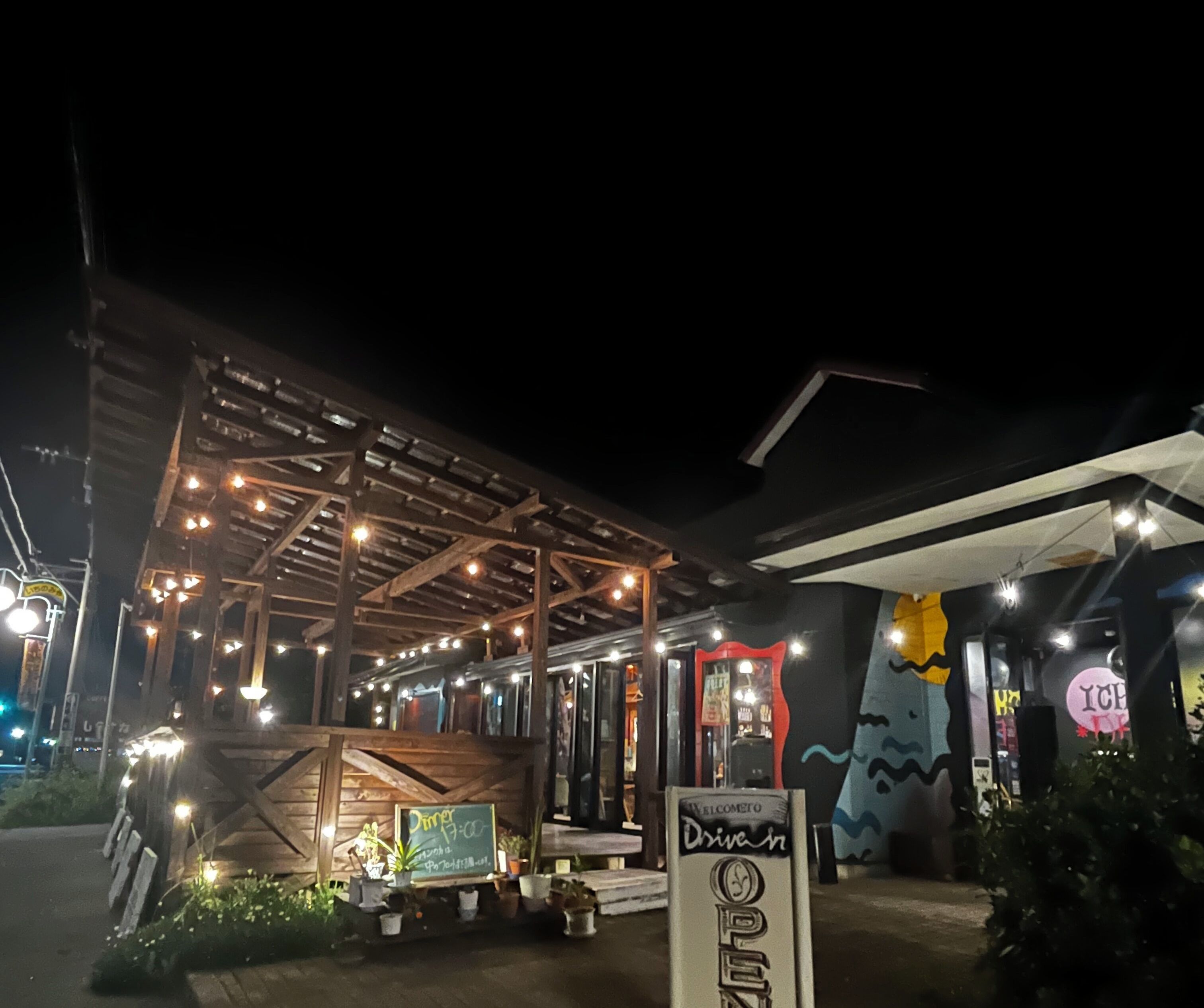 A wooden outdoor seating area with string lights, a chalkboard sign, and a welcome sign.