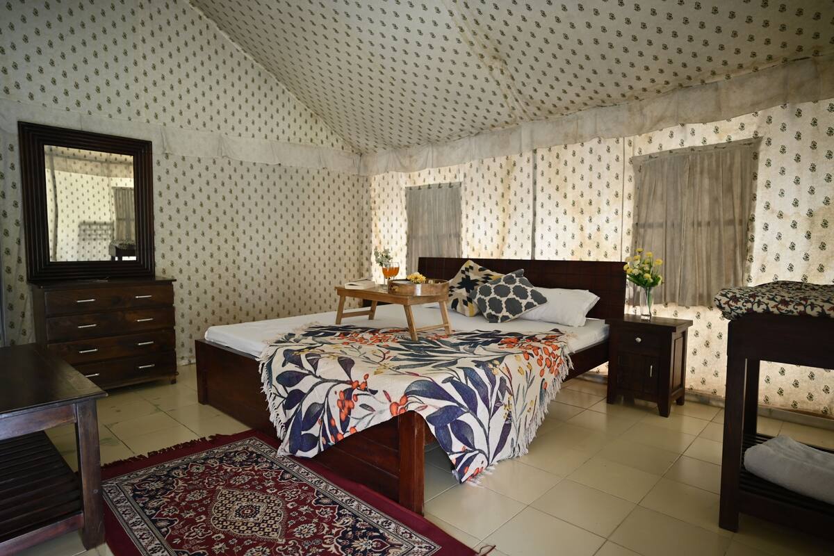 A bedroom with a bed, a dresser, a nightstand, a mirror, and patterned wallpaper.
