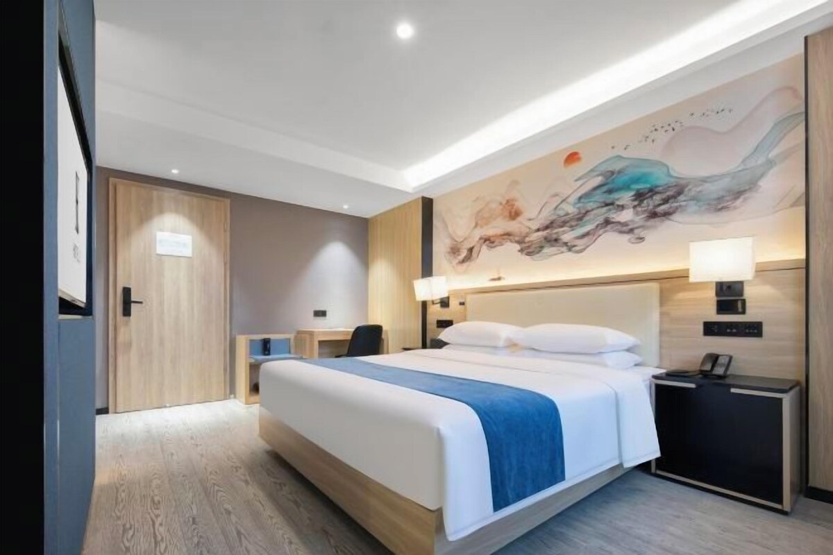 A modern hotel room with a large bed, a desk, and a nightstand.
