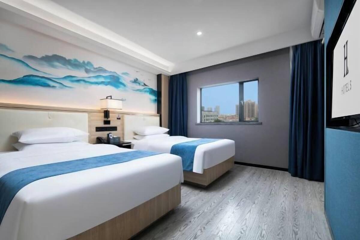 A hotel room with two beds, a city view, a painting on the wall, and a TV on the wall.