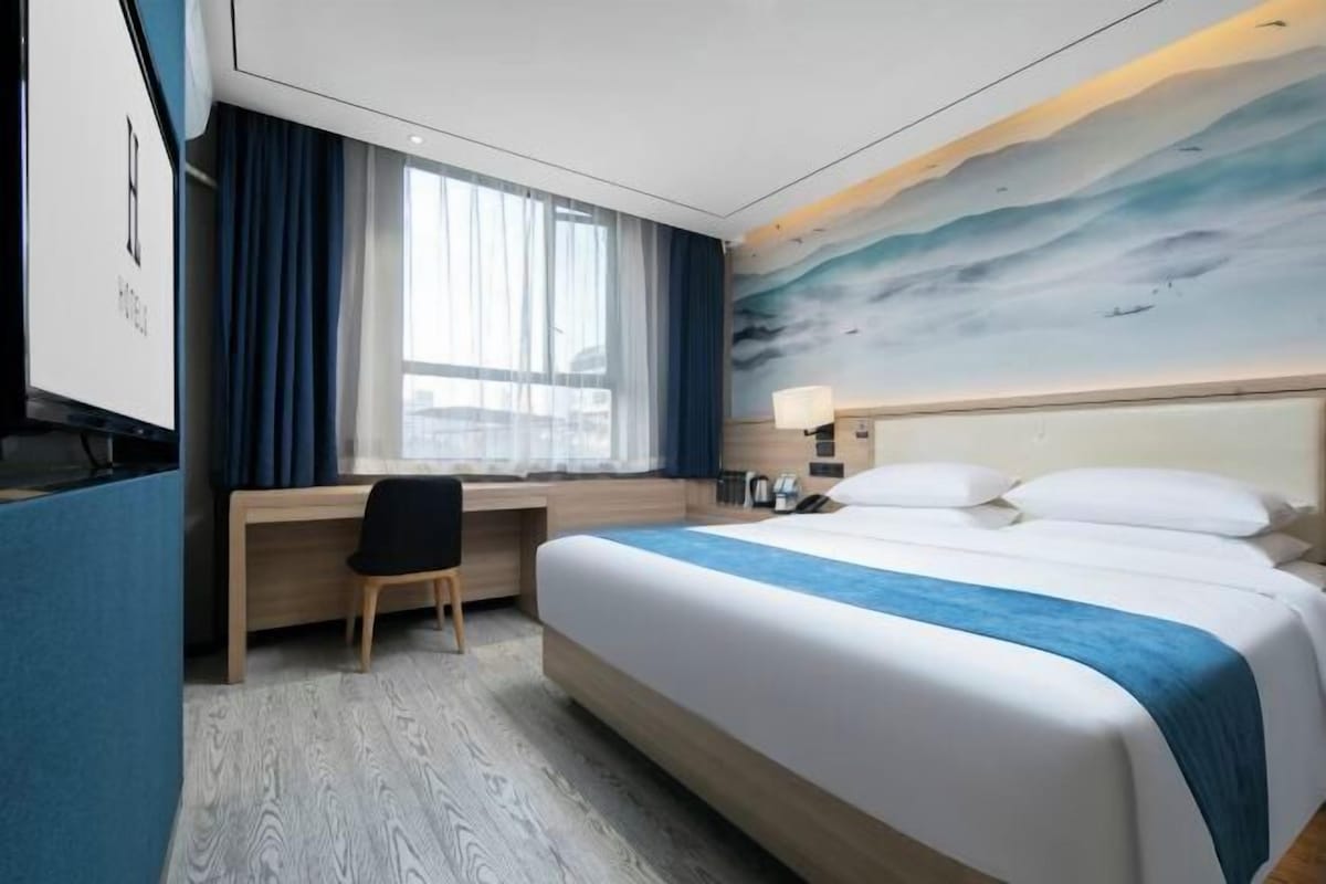 Una habitación de hotel con cama, escritorio, silla y un ventanal con cortinas.