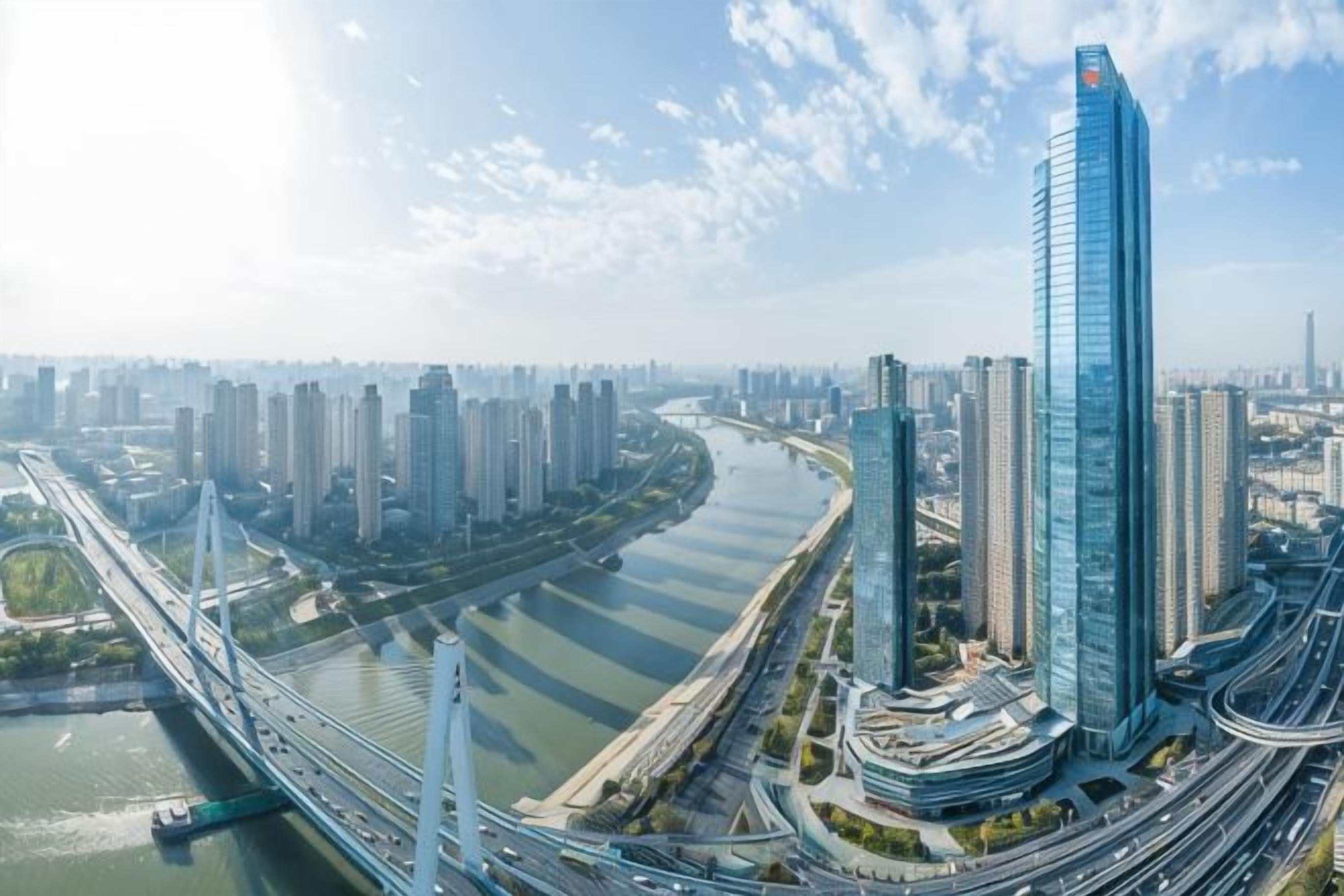 Un immeuble de grande hauteur doté d’une façade moderne en verre, situé dans un environnement urbain dense, entouré d’autres immeubles de grande hauteur et bordé par une rivière.