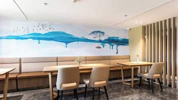 Un espace repas moderne agrémenté d’une fresque murale, de sièges et offrant une vue sur l’extérieur.