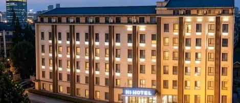 Un hotel de varios pisos con un llamativo letrero 'Hi Hotel', un frente bien iluminado y un diseño arquitectónico moderno.