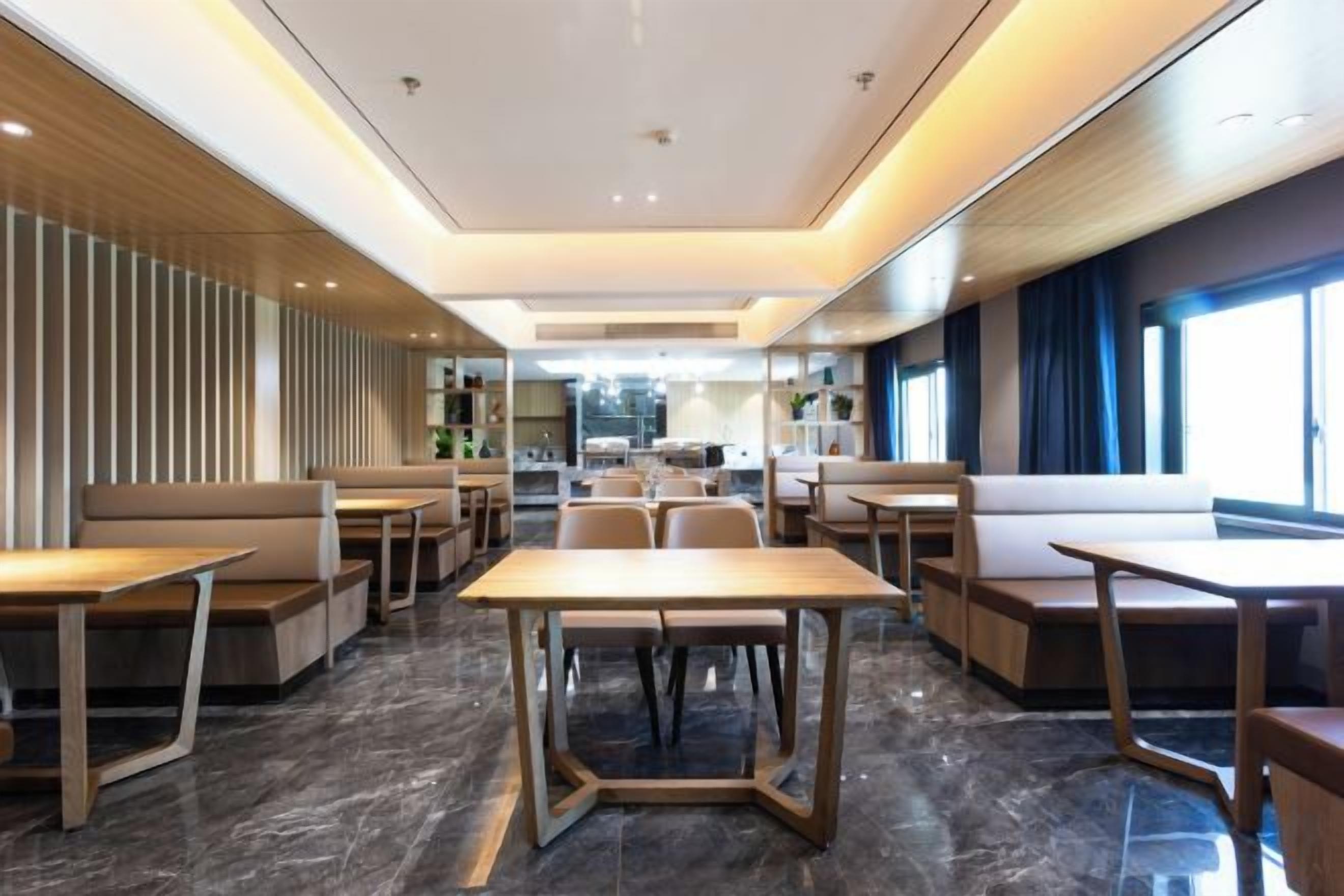 A modern hotel lobby with seating areas, a central table, and a kitchen in the background.