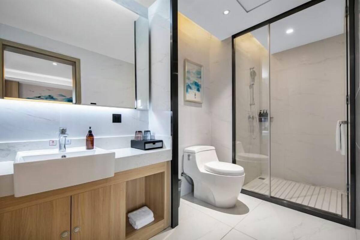 A modern bathroom with a white sink, mirror, and toilet. It includes a shower area with glass doors.