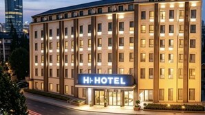 Un hotel de varios pisos con un llamativo letrero 'HI HOTEL', una fachada limpia y una entrada bien iluminada.