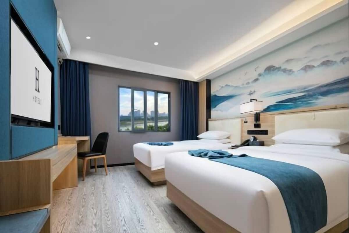 A hotel room with two beds, a desk, and a large window.