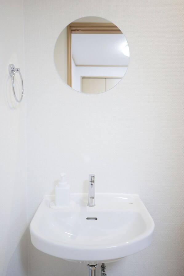 A white bathroom sink with a mirror above it. - KARAHORI NODOKA (Osaka)