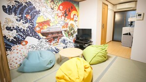 A room with tatami flooring, a futon bed, a television, and a wall mural. - KARAHORI NODOKA (Osaka)