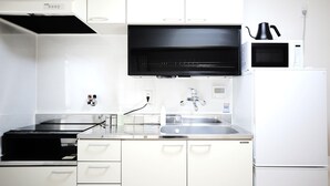 A modern kitchen with white cabinets, a black range hood, a stainless steel sink, and a white refrigerator. - KARAHORI NODOKA (Osaka)
