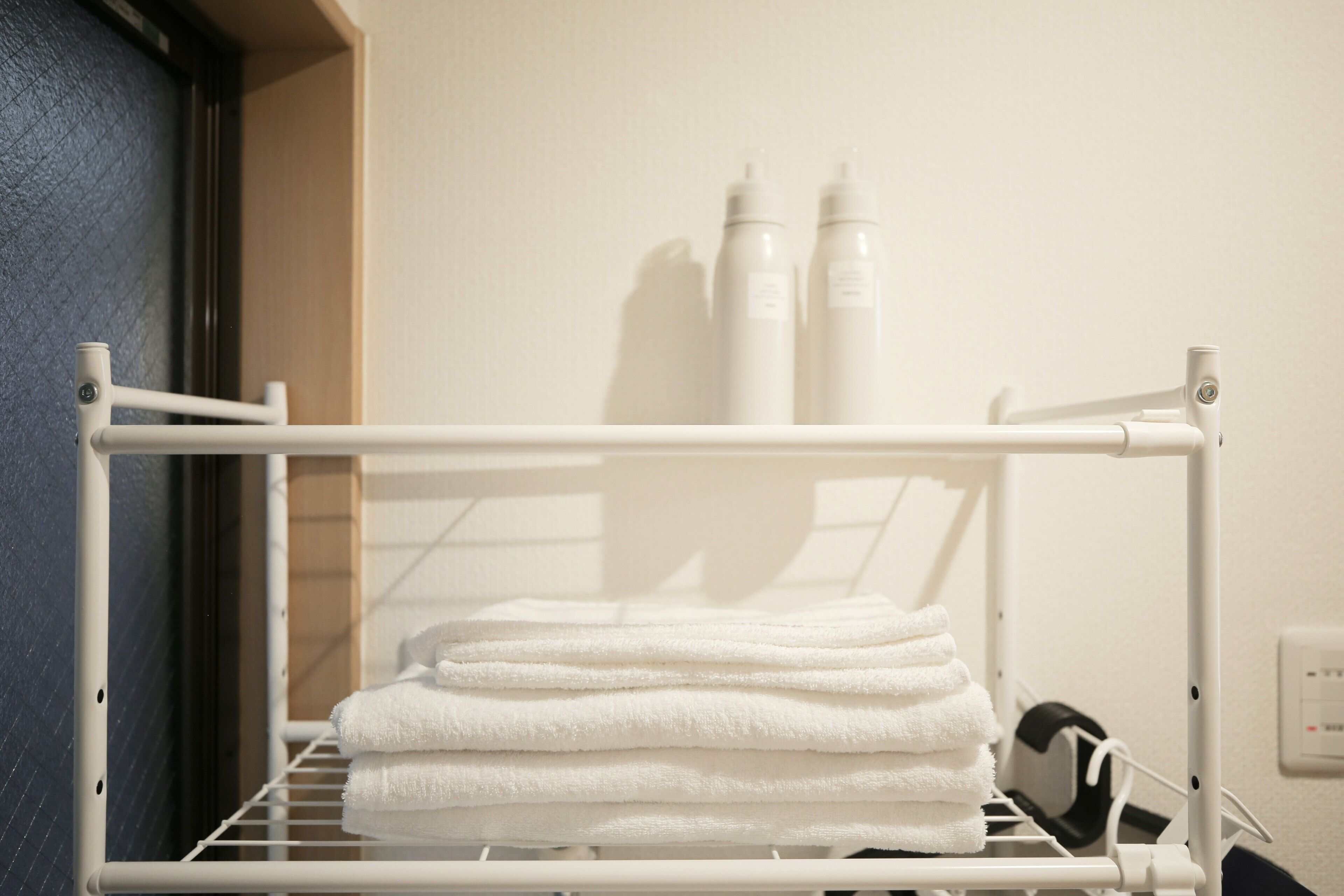 A white towel rack with folded towels and two bottles in the background.