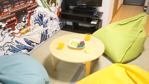 A room with a round wooden table, a television, and colorful cushions. - KARAHORI NODOKA (Osaka)