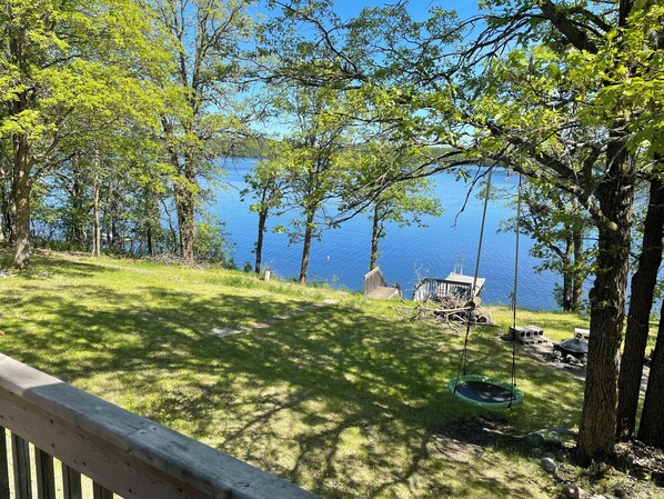 A lakeside view with a wooden deck, a swing, and a small dock extending into the water.