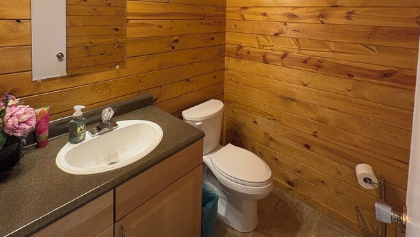 Une salle de bain aux murs lambrissés, équipée d’un lavabo, d’un miroir et de toilettes.
