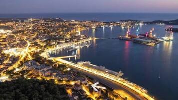 An aerial view of a coastal city at dusk with a prominent bridge and a large cruise ship docked at the port.